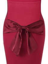 A close-up of the TIGERMIST ZITA DRESS - RED : SALSA : DEEP RED, a bodycon maxi dress detailed with a large, shiny satin waist bow.