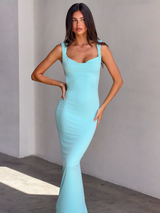 A woman wears the TIGERMIST MORANA DRESS in sky blue, featuring a scoop cowl neck and maxi length.