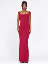 A woman stands against a white background wearing the TIGERMIST ZITA Dress - Red : Salsa : Deep Red, a sleeveless bodycon maxi dress with a slight cowl neckline, styled with black open-toe heels and her dark hair in a center-parted updo.